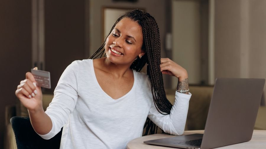 A smiling woman holding her credit card while shopping online on a laptop
