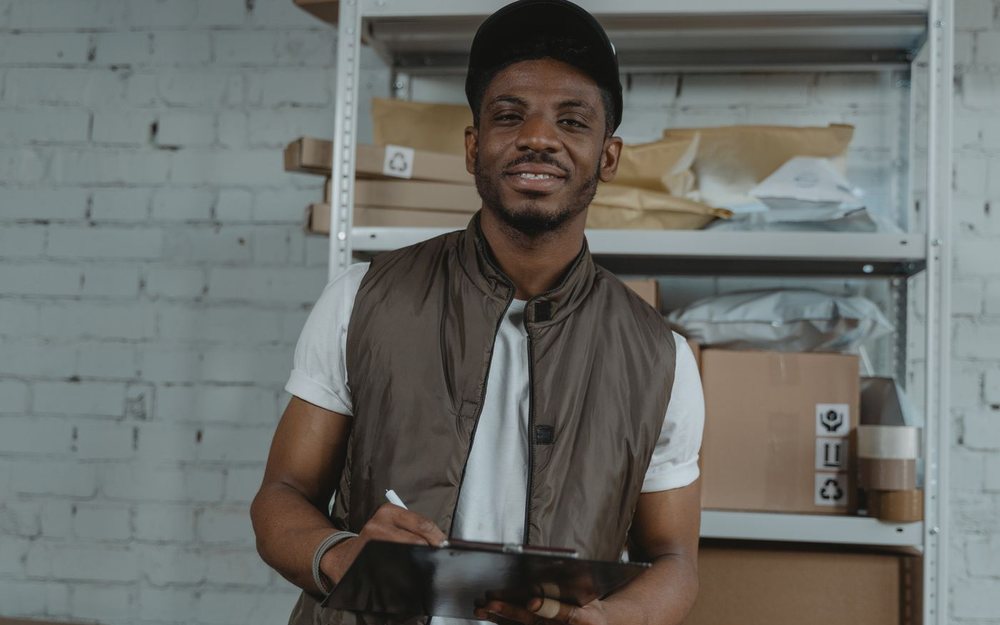 A smiling warehouse manager with a clipboard checking stock on the shelves