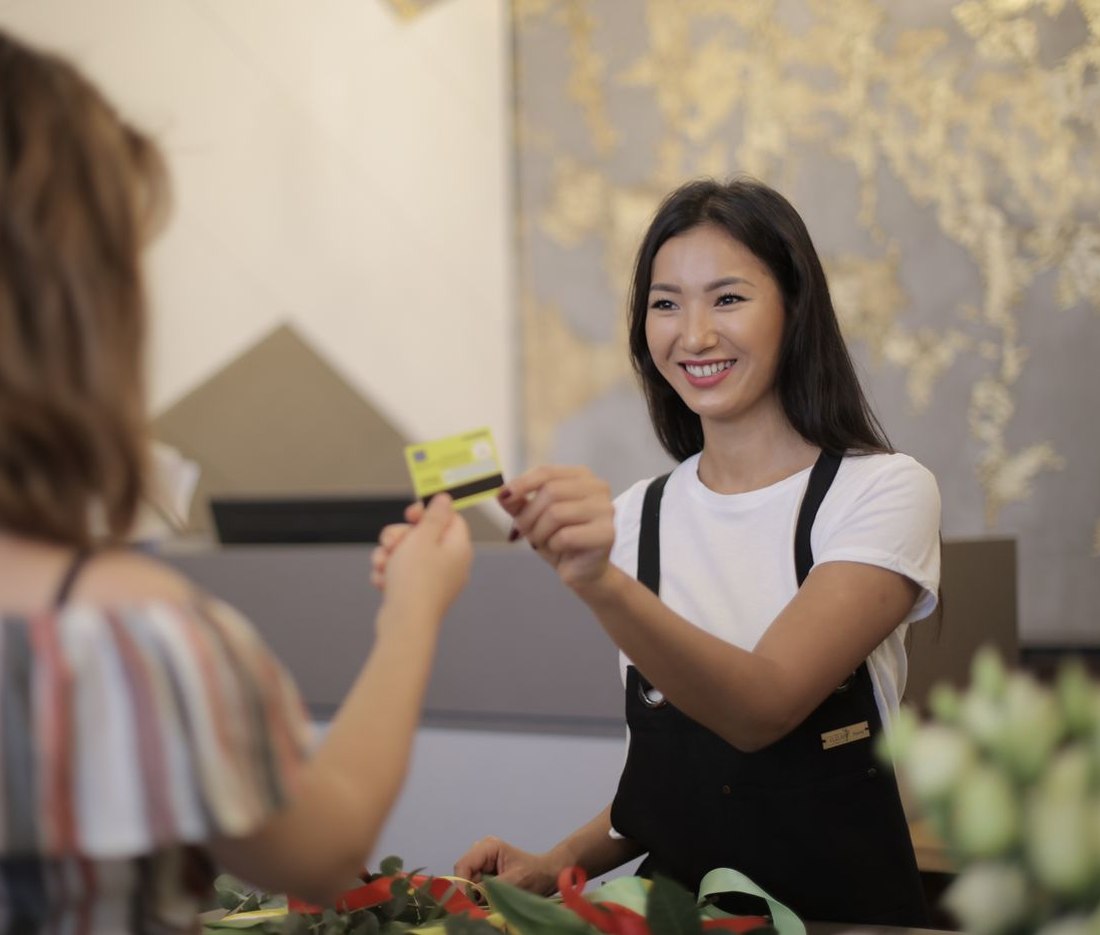 A smiling shop owner taking a customer's credit card at the counter