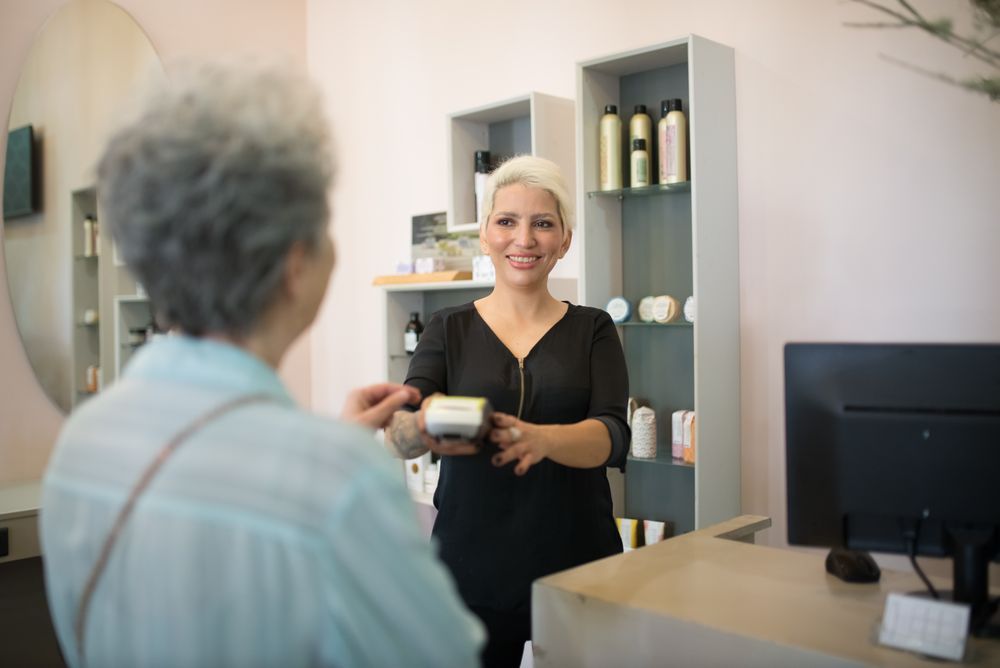 A stylist helping a client pay at a salon front desk
